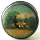 A cheerful small snuff box decorated with a painting over a print of a couple drinking in the open. An unusually earthly subject, suitably executed. English, circa 1810. 