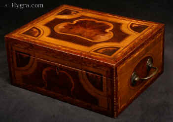 JB431: A rare and striking box made by a gifted craftsman who had a truly artistic instinct for the materials at his disposal. Patterns are created by different woods, which mutually enhance and compliment the varied qualities of the timbers, resulting in an object the beauty of which is wholly created by projecting organic natural growth. The faint straight grain of the background veneer is an unobtrusive background which allows the dramatic centre to make a bold and striking statement: the force and beauty of a living plant. The box has a replacement tray with supplementary lids. Circa 1790. Enlarge Picture