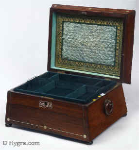 Rosewood veneered box in neoclassical form circa 1835. A box inspired by the shapes of classical temples fashionable in the second phase of neoclassicism. The structure with its angled and tiered sections gives the impression of elegance and strength. The decoration in mother of pearl and white metal is restrained. It further emphasizes the strength of the lines and enlivens the colour of the wood. The escutcheon and central motif in controlled stylized flora give a note of softness. The original lift-out tray has been re-covered in cotton velvet. The inside of the lid is covered in the original ruched silk surrounded by gold-embossed leather. The handles are original albeit with some old breaks and repairs. The feet are not original. Working lock and key. Enlarge Picture