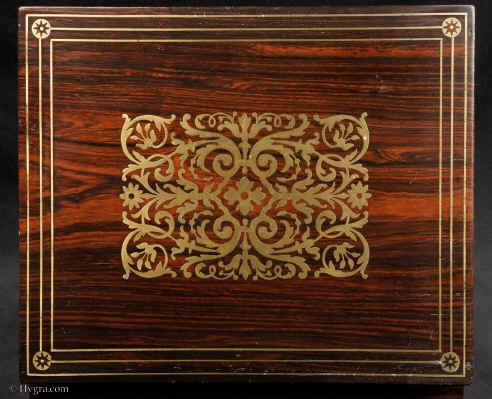 JB505:  Rosewood  box which combines style with elegance. The thick saw-cut veneers of the rosewood are selected for the rich figure of the wood which is contrasted with the brass inlay.The design is controlled in deference to the Georgian neo-classical tradition but it also embraces the Regency influence of the Royal cabinet maker George Bullock, who introduced naturalistic elements to the earlier austere brass designs. Circa 1825 Enlarge Picture