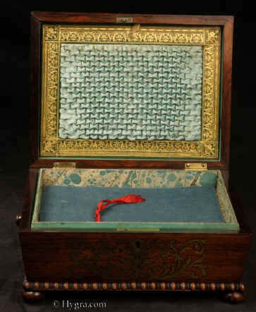 JB511: Antique box in the sarcophagus form. The box is veneered in figured rosewood and is inlaid in brass depicting stylized flora.  The fluid design of stylised flora is exceptionally fine. This is a spectacular box which encapsulates the best of the Regency era. The box stands on turned rosewood feet and has turned rosewood drop ring handles. The centre panel of the top is framed with gadrooning as is the pediment adding the architectural impact. The box has a lift out tray which has been relined . Circa1825. Enlarge Picture