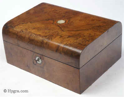 SB459: Burr walnut veneered box of rounded form, circa 1870. A box veneered in particularly well figured burr walnut. It is sparsely decorated with hexagons of mother of pearl subtly cross banded and framed in lines of contrasting woods. The tray, three silk covers and ruched back are original. The darker covers are of later velvet. Working lock and key.   Enlarge Picture