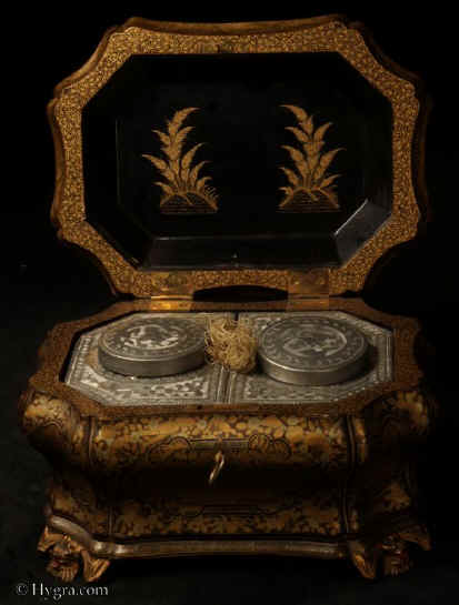TC581:A curvaceous Chinese export lacquer tea chest with undulating sides decorated with two colours of gold depicting scenes of of Oriental life opening to a single compartment containing two lidded pewter tea canisters with supplementary inner lids, the whole chest standing on feet in the form of dragon heads. Circa 1840. Enlarge Picture