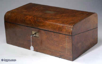 WB169: A rounded top writing box in figured burr walnut having brass escutcheon and plate opening to an embossed velvet writing surface and compartments for writing implements and paper. The facings are in coromandel. The box has two hand made replacement inkwells with screw tops. Circa 1860. Enlarge Picture