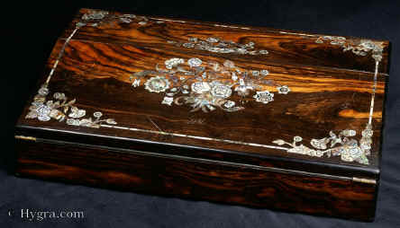 WB464: Writing slope veneered in saw cut coromandel inlaid with engraved mother of pearl and abalone by Mapin of London and Sheffield. Circa 1845. This is a stunning slope, the dark wood with waves of golden figuring, decorated with floral designs in mother of pearl and abalone shell. The shells are selected so that their colour and iridescence contribute to the artistic appeal of the whole. The white flowers surrounded by green stems and leaves. The petals and leaves are further defined by engraved lines. Unlike the earlier neoclassical designs, the flowers are recognisable, although there is an eccentric note in a bud within a flower in the central bouquet; a quirky note in a naturalistic design. The interior continues the high quality with abalone lines giving an iridescent outline to the coromandel outline and lids. There are two original silver plated inkwells. The writing surface is covered in a replacement gold embossed leather. Under the flap there is highly iridescent satinwood. Unusually for a slope there are also secret drawers in coromandel and satinwood. Working lock and key.
  Enlarge Picture
