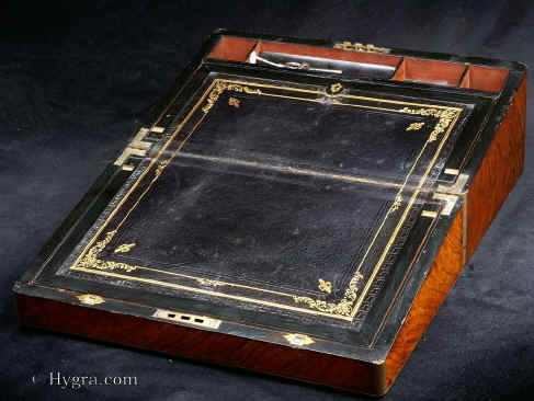 WB465: Writing box veneered in walnut circa 1875. Writing box veneered in figured walnut with rounded brass surround and fine brass stringing. The brass acts both ad decoration and protection. The interior is veneered in ebonised wood. The writing surface is covered in the original gold embossed leather. There is a second lock to the flap and two secret drawers.  Enlarge Picture