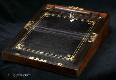 WB466: Writing box veneered in richly figured walnut dated 1892. This box is veneered with striking pieces of wood, the centre of the top is burr encircled by wavy figure. The box is strengthened and enhanced with rounded brass and accented with fine brass lines. It has a strong Bramah lock. The box is veneered inside with ebonised wood. It has a second lock on the flap. The writing surface is covered in the original gold embossed leather. There are two reproduction inkwells. There are two secret drawers. Working locks and keys. Enlarge Picture