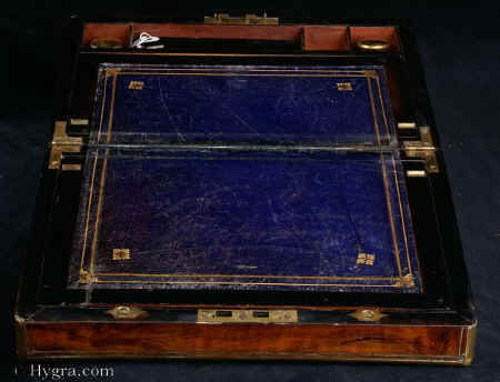Writing box veneered in figured walnut circa 1880:  Writing box veneered in figured walnut, with rounded brass surround and brass lines. Strong Bramah lock. Inside the box is veneered in ebonised wood. The writing surface is lined in the original blue gold-embossed leather. The inkwells are added (new). The flap lifts to a mahogany interior. There are two secret drawers. Working lock and key.<br>
              Enlarge Picture