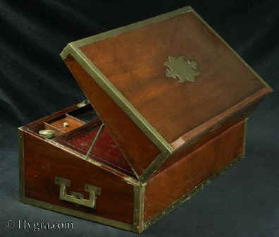 WB482: High quality  Regency brass edged mahogany writing box in the military style, with countersunk brass handles opening to embossed leather (replacement) writing surface and compartments for pens and inkwells, having compartments for paper under the flaps. The box also features a mechanism so that it can be used as a reading stand or lectern. There are three secret drawers concealed behind a sprung panel. The box retains two original inkwells with screw tops.  Circa 1810. Enlarge Picture