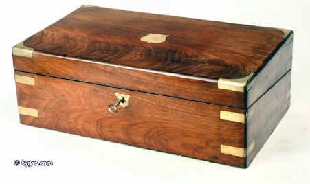 wb142:  Antique flame mahogany writing box with brass corners and straps, working lock and key opening to a sloped velvet covered writing surface and compartments for pens and writing implements. Under the flaps there are compartments for holding paper. The box also has secret drawers hidden behind a sprung panel which is released by pulling up one of the divisions in the pen compartment. circa 1840. Enlarge Picture