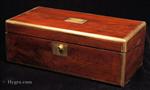 A Victorian writing box veneered in figured flame mahogany with rounded brass surround and fine brass stringing  The main lock is Bramah. The brass acts both as decoration and protection. The interior is veneered in ebonised wood. The framed writing surface is covered in a replacement gold embossed leather. There is a second lock to the upper flap.   Three secret drawers  are hidden by a sprung panel beneath the compartments for writing accessories and inkwells.